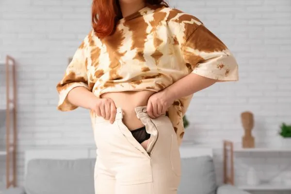 Image of woman trying to do her trousers up after pregnancy weight gain Maplehurst